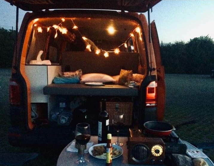 Interior de furgoneta camper con luces, transmite tranquilidad. En el plano delantero una mesa lista para cenar.