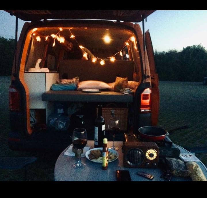 Interior de furgoneta camper con luces, transmite tranquilidad. En el plano delantero una mesa lista para cenar.