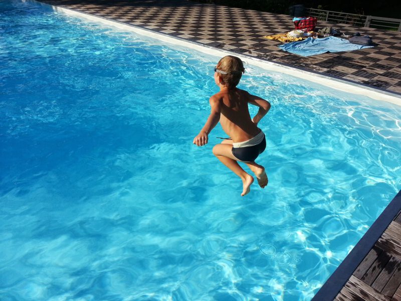 Un niño pequeño salta al agua en una piscina. Seguro de responsabilidad civil para proteger a tus hijos en las piscinas.