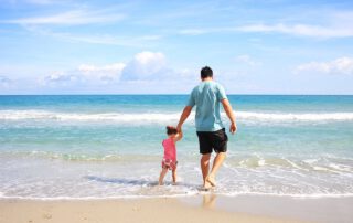 Un padre con su hija caminan por la playa frente al mar. Cinco razones por las que contratar un seguro de vida.