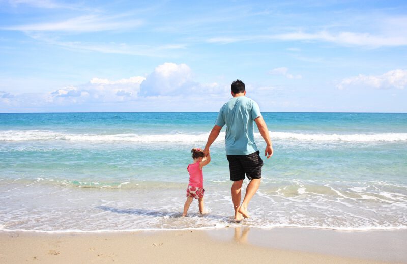Un padre con su hija caminan por la playa frente al mar. Cinco razones por las que contratar un seguro de vida.