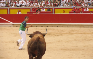 Recortador esquiva al toro durante un festejo taurino en una plaza de Toros de Pamplona con público.