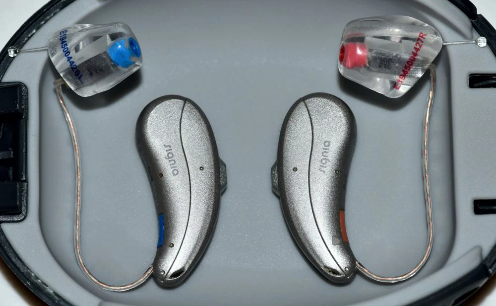 Dos audífonos retroauriculares colocados en su estuche, dispositivos que pueden protegerse con el Seguro de Audífonos de Segur Torralba.